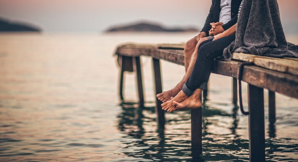 Image of couple sitting on a dock with lake in background.