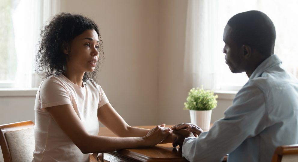 How to inspire your partner to join you in couples therapy. Image of couple talking while holding hands and looking at one another.