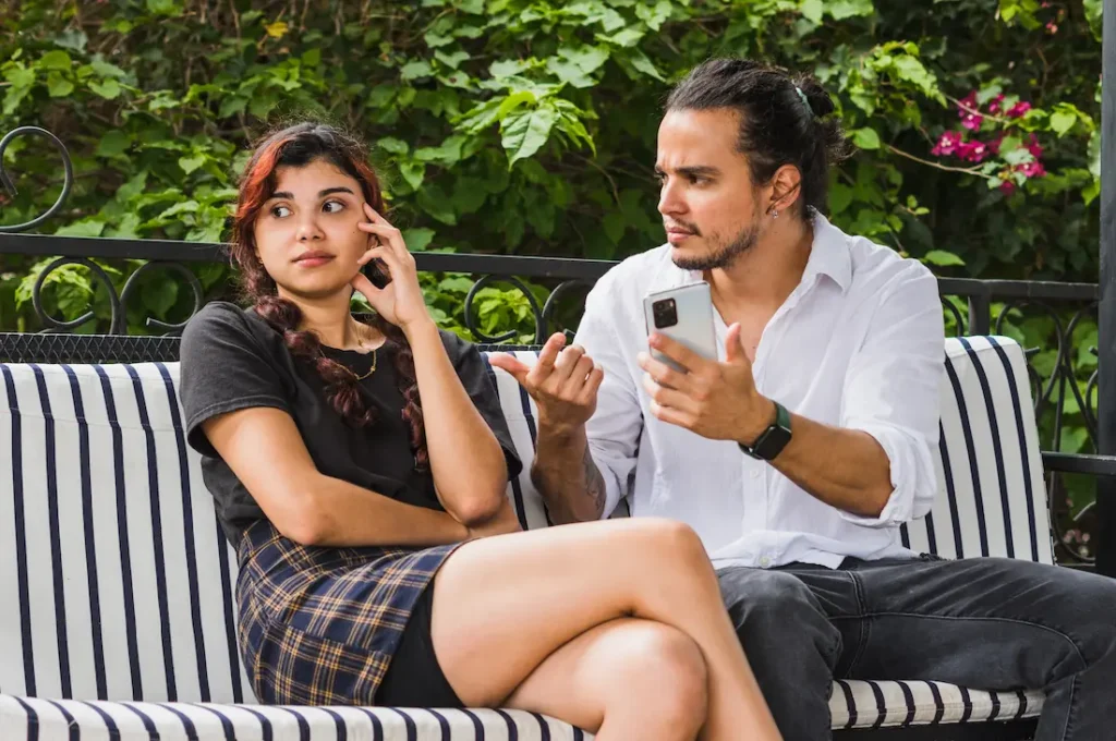 a young couple sitting on a park bench, one is confronting the other showing how jealousy in a relationship can manifest