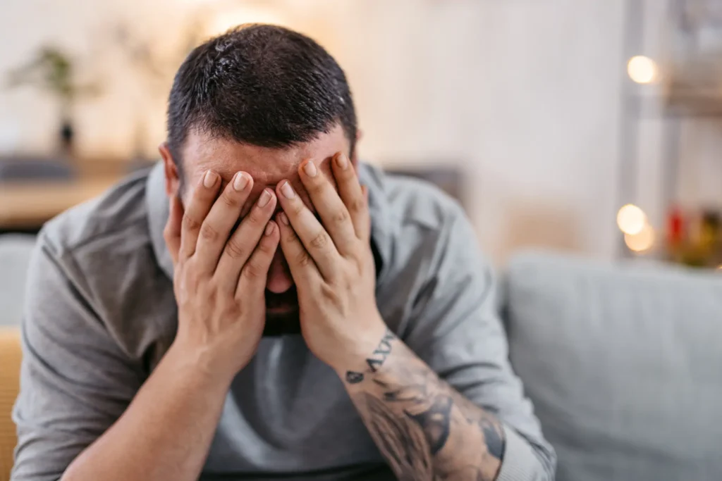 Man sitting with hands covering his face dealing with shame.