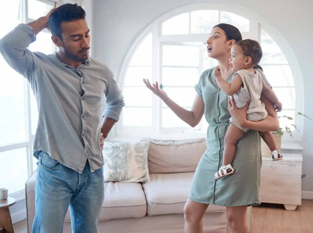 Nagging in a relationship is shown as a wife nagging her husband about a chore while holding their baby.
